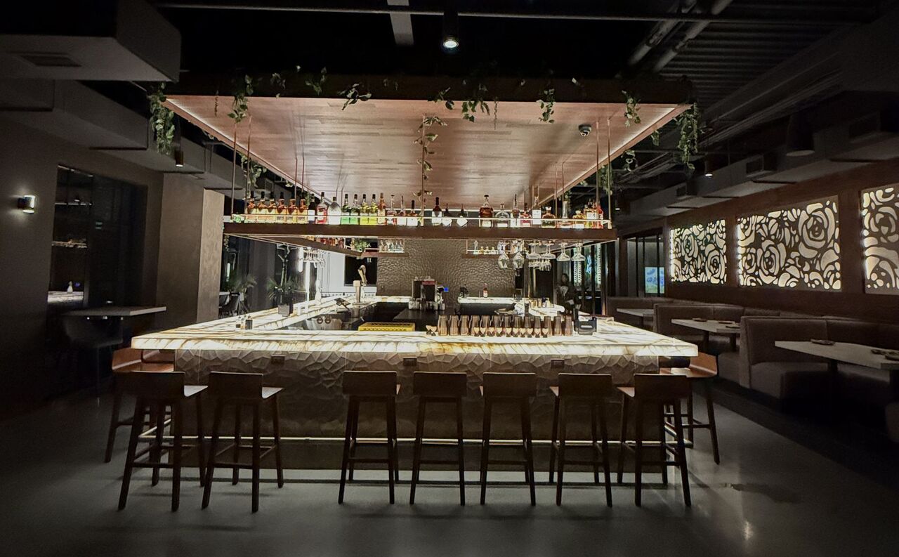 The bar at Kasi in Brighton, Michigan, a backlit onyx bar top glowing under a suspended wood canopy