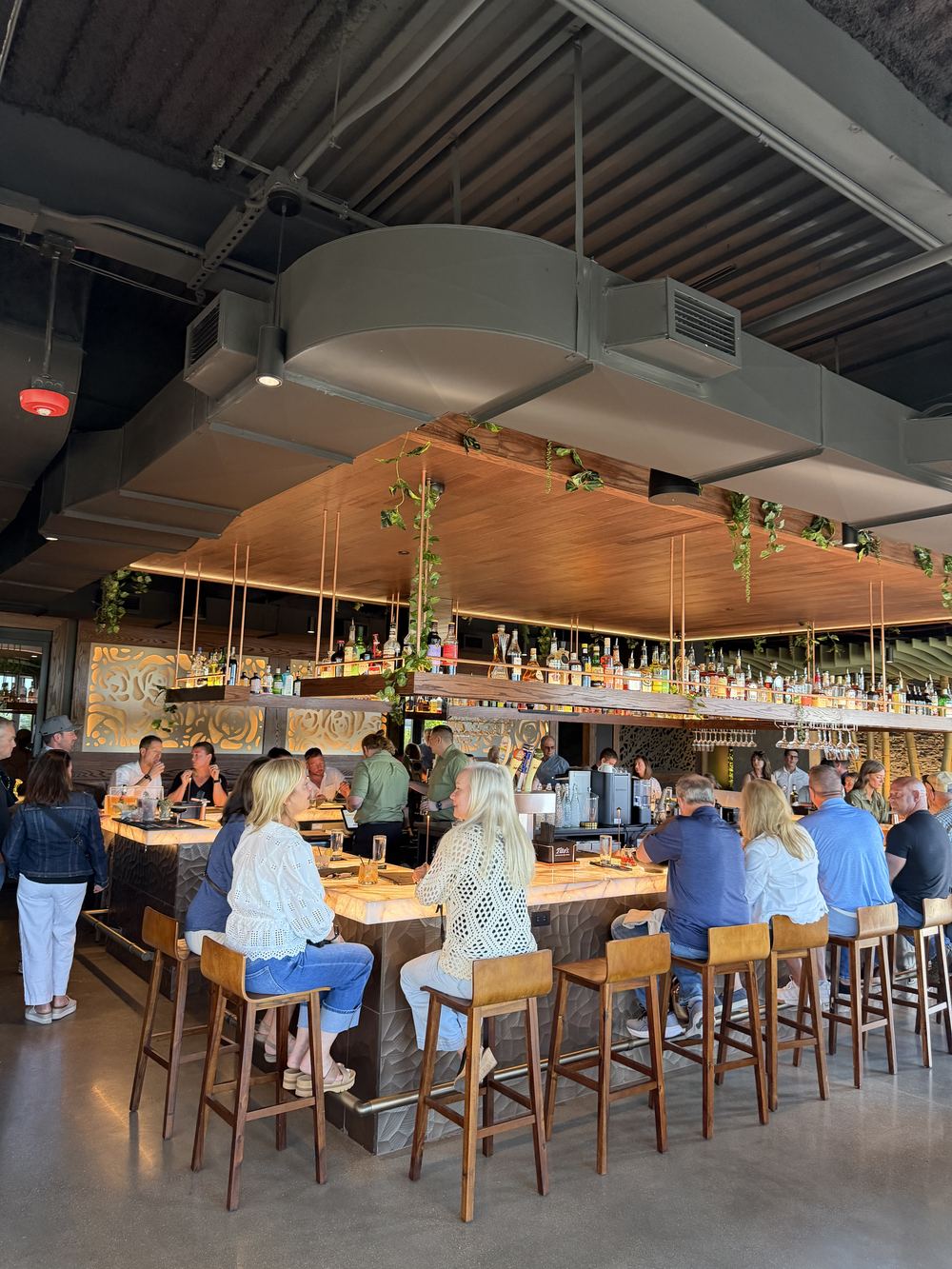 Guests seated shoulder to shoulder around the Kasi bar during a busy afternoon service