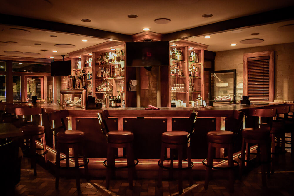 The full Zynda's bar shot head on before service, wooden stools set around the bar under warm light