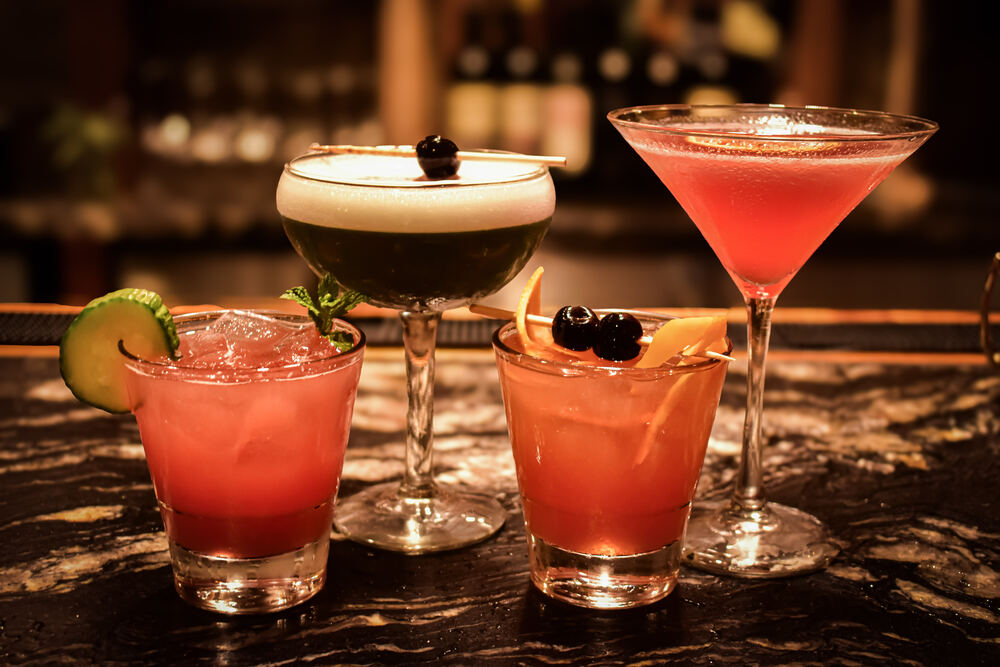 Four Zynda's cocktails lined up on the bar: a cucumber cooler, a foam-topped coupe, a garnished rocks pour, and a cosmopolitan